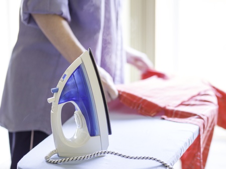 Woman ironing a red shirt with a steam iron taken against a bright, airy background の写真素材