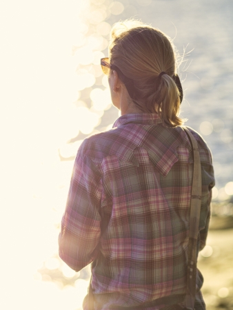 Woman standing at the edge of a bay staring out at the water while thinking or relaxing.の写真素材