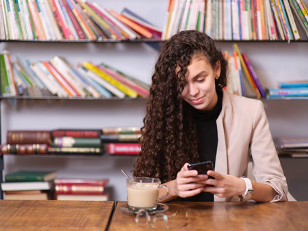 young woman checking her mobile phone while sitting with a hot drinkの写真素材