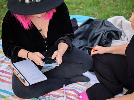 woman looking at her mobile phone sitting in the park with a friendの写真素材