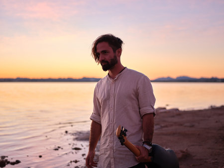 man gazing intently ahead, holding his guitar in one hand, nightfall on the lake