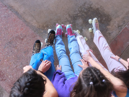 Top view of three young woman sitting while wearing classic skates outdoors