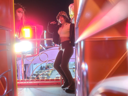 Friends dancing on a fairground attraction illuminated by neon lights at nightの写真素材