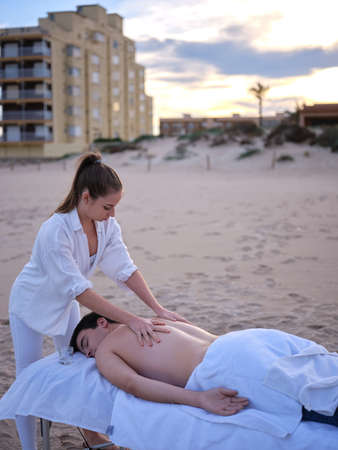 A young chiromassage therapist giving a massage to young adult man to treat his back injury on a beach in Valencia at sunset.の写真素材