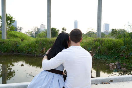 Back of a couple embraced while looking to the sunset in an urban parkの写真素材