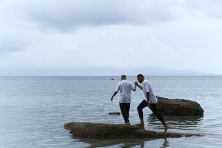 Gay couple jumping between rocks in the middle of the sea during twilight