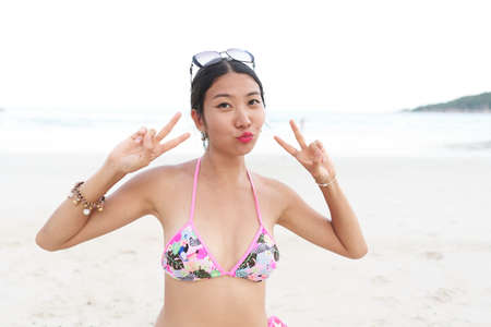 Asian woman gesturing victory with the fingers on a beachの写真素材