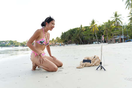Asian young streamer sitting on the beach while performing live on mobileの写真素材