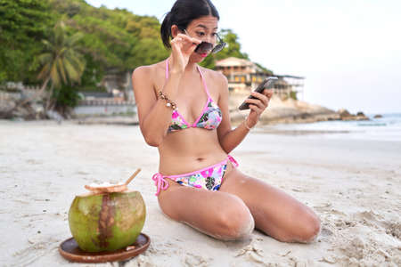 Streamer taking off his glasses to read his mobile screen on a beachの写真素材