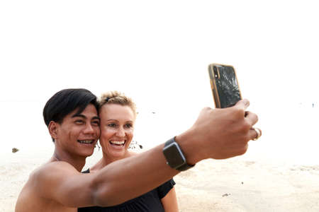 Multicultural couple taking a selfie with a mobile on the beachの写真素材