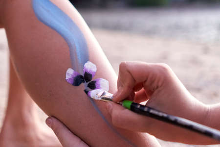 Artist painting a flower in the leg of a woman in the beach