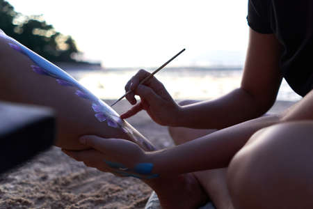 Artist painting the body of a woman during sunset on a beachの写真素材
