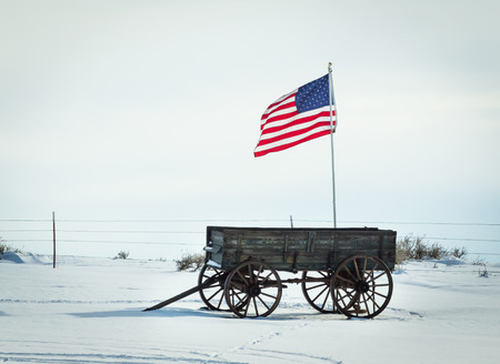 An American flag flies above an antique wagon.の写真素材