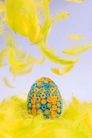 Funny, amusing and joyful photo of yellow and blue Easter egg lying in yellow feathers, visible...