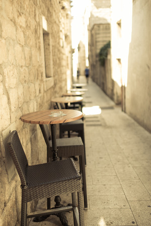 Narrow street of old town with old sandstone buildings, in foreground caffee table and chairs, outdoor photo の写真素材