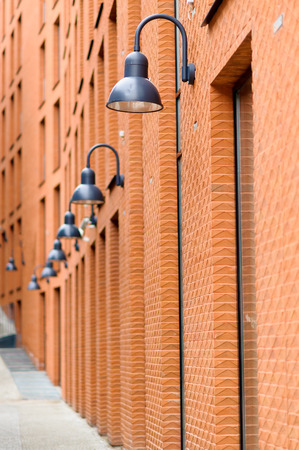 Frontage of modern red brick  building ith visible fragments of windows and black street lamps, linear perspective の写真素材