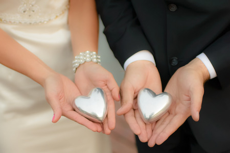 Man and woman, elegantly dressed, wearing wedding clothes, holding symbolic silver hearts in their hands, softfocus, visible unrecognizable fragments of body, model release not required の写真素材