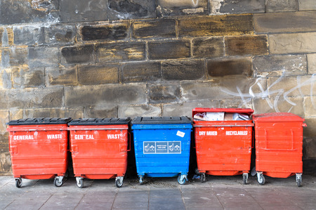 One blue and four red  street dustbins, litter bins,  rubbish bins, visible fragment of brick wall の写真素材