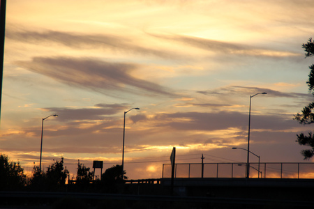 Sunset view at Fremont, California, USA with golden skyline and darker cloud patches along the horizon with few clear opening, power lines and poles in foreground.の写真素材