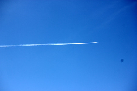 Jet smoke trail in blue sky gradually expanding and merging with the sky over period of time.の写真素材