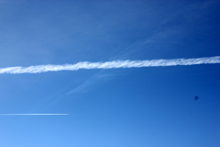 Jet smoke trail in blue sky gradually expanding and merging with the sky over period of time.の写真素材