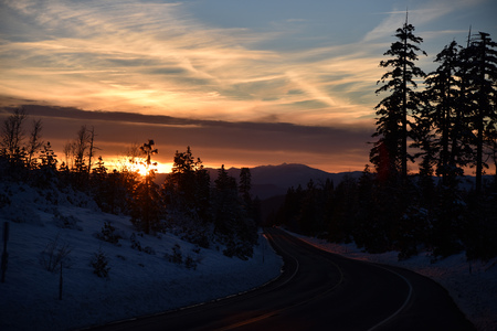 Sunset view from Shasta Road on Christmas day, snow covered slopes and pine trees, orange clouds above mountains and blue sky.の写真素材