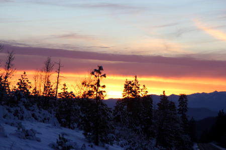 Sunset view from Shasta Road on Christmas day, snow covered slopes and pine trees, orange clouds above mountains and blue sky.の写真素材