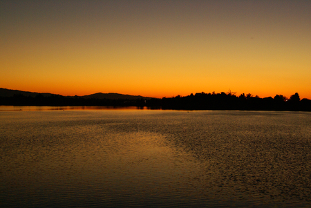 Sunset View at Shoreline Park Lake, California, USA , dark undulating mountain line, orange yellow sky at horizon, fading into gray above and its reflection in the lake water.の写真素材