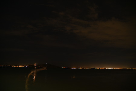 Night view of San Francisco Bay, California, USA, with city lights, hills and partial clouds in the distance.の写真素材