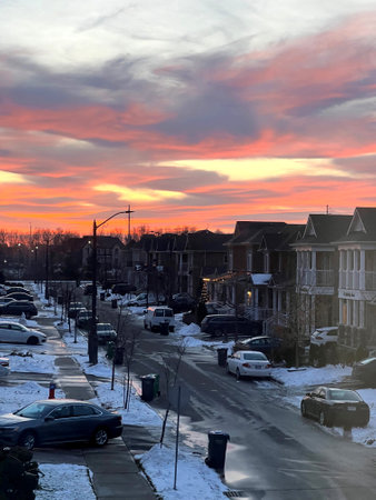 Sunset at Brampton Canada on a wintry evening with golden, yellow and dark grey clouds above the trees and buildings, snow covered streets in foreground.のeditorial素材