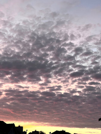 Sunset in Fremont, California early March with scattered dark clouds over the horizon broken up by light red sky above the street buildingsの写真素材