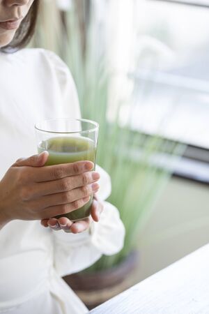Hand of young woman with green juice poured into glass