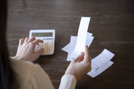 Hand of a young woman who looks at the receipt and does accountingの写真素材