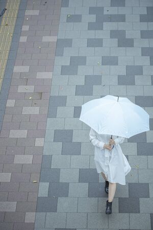 A young woman in a white dress walking with an umbrella in the rainの写真素材