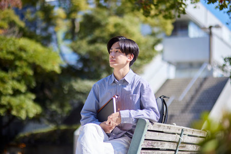 Japan university student sitting on a bench on university campusの写真素材