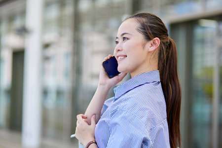 Smiling Japan businesswoman making phone calls on smartphoneの写真素材