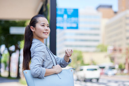 Business woman waiting for a bus at a bus stop in summerの写真素材