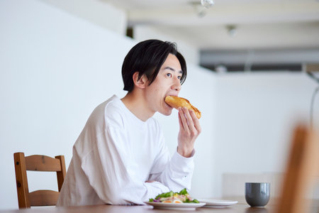 Young Japan man eating breakfast in living roomの写真素材