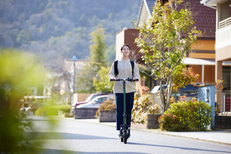 Japan woman moving on an e-scooter in a residential areaの写真素材