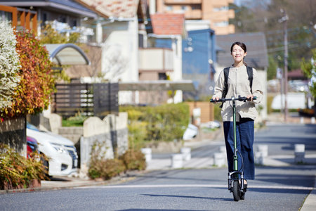 Japan woman moving on an e-scooter in a residential areaの写真素材