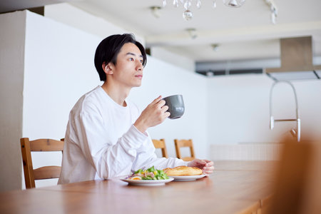 Young Japan man eating breakfast in living roomの写真素材