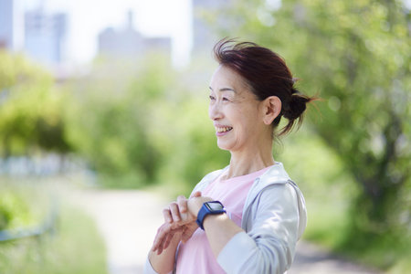 Senior woman wearing sportswear measuring with a smartwatch in the fresh greenery of springの写真素材