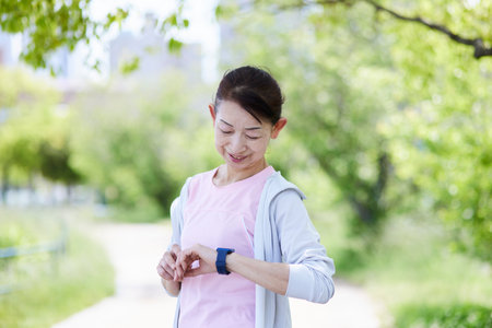 Senior woman wearing sportswear measuring with a smartwatch in the fresh greenery of springの写真素材