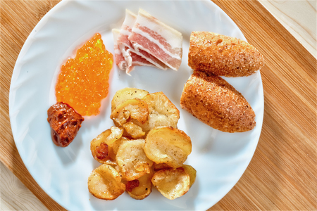 Tasty unhealthy food. Greasy fried potatoes, bacon, red caviar, spicy sauce and white bread on a...