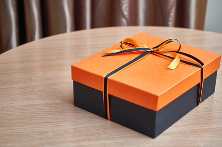An elegant black box with an orange lid for a gift tied with a black and orange ribbon with a beautiful bow.の写真素材