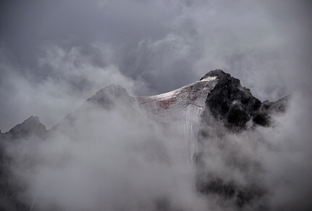 Severe winter snow-capped mountains in the fog and clouds.の写真素材
