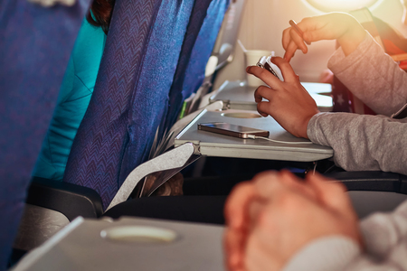 Using a smartphone while traveling by plane. Girl presses her fingers on the screen of the phone.の写真素材