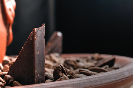 Piece of black chocolate in roasted coffee beans on a clay dish.  Rays of light.の写真素材
