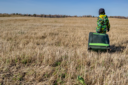 Child with the suitcase goes through a big yellow autumn field. Rear view.の写真素材