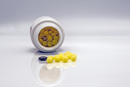 Colorful medications and pills. Close-up of a pile of yellow round tablets and one gray tablet on the background of a plastic medicine bottle.の写真素材